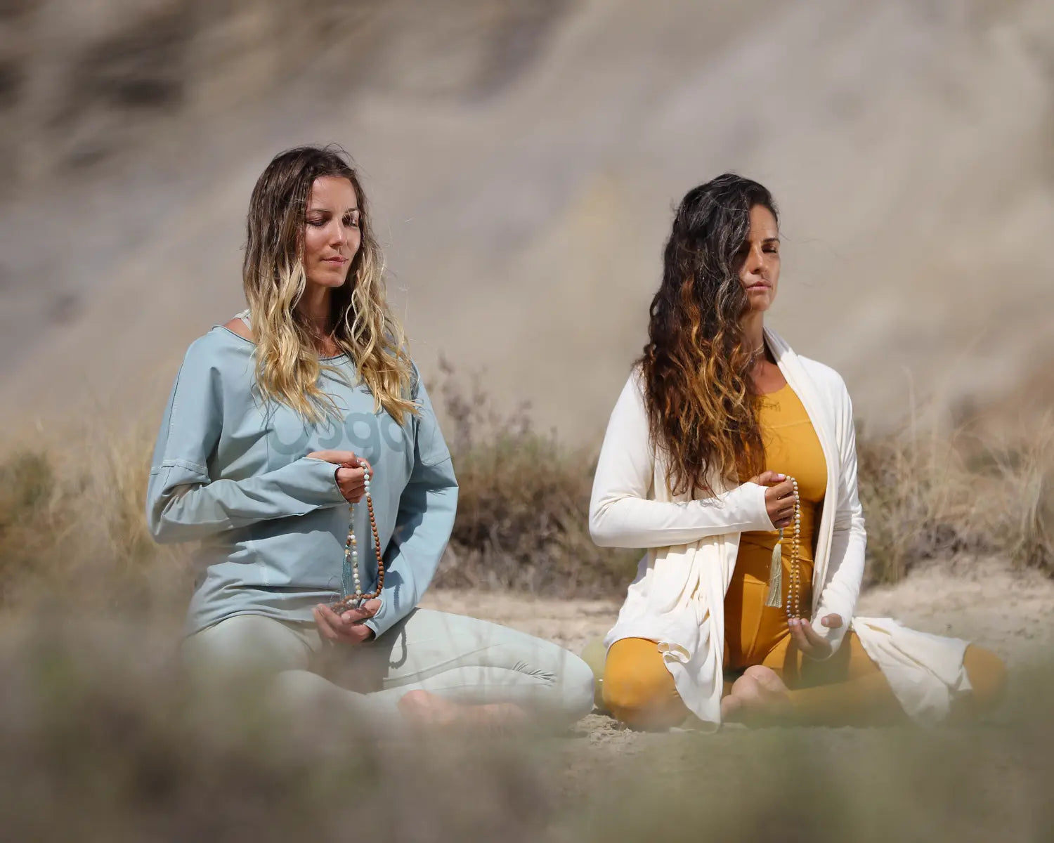 Alinear chakras: beneficios y paso a paso con Yogimi. Dos mujeres meditando con malas en un entorno natural, símbolo de equilibrio y armonía interior.